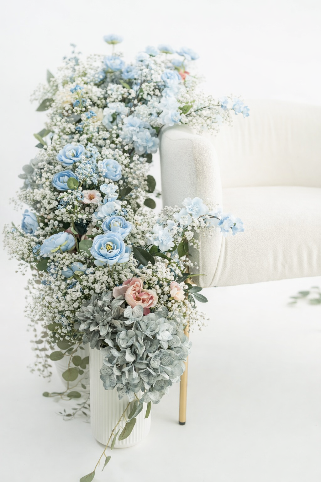 Delicate floral arrangement with light blue roses, baby's breath, and eucalyptus leaves in a clear glass vase.