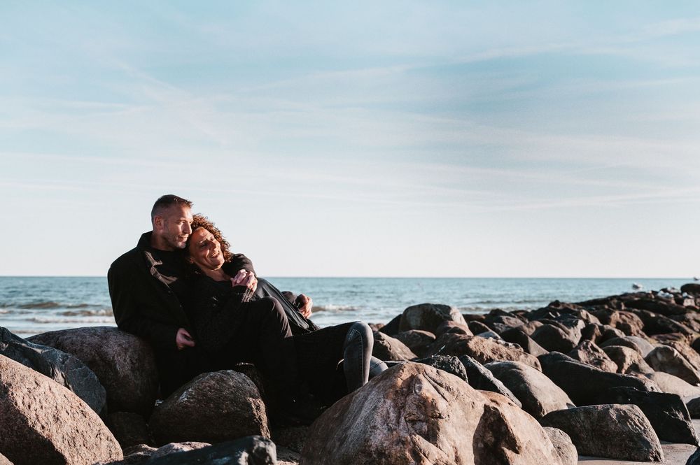 Paar sitzt eng umschlungen auf einem Felsen am Strand, farbiges Outdoor-Foto