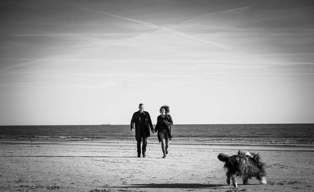 Pärchen hält sich am Strand in Dänemark an den Händen, lachend im Sand