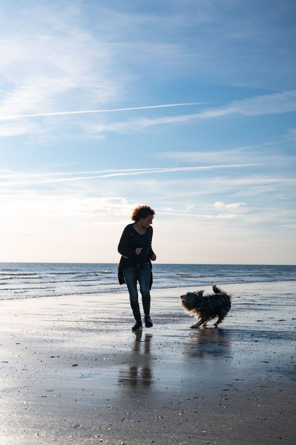 Frau rennt lachend mit ihrem Hund im Gegenlicht am Strand in Dänemark, farbiges Outdoor-Shooting