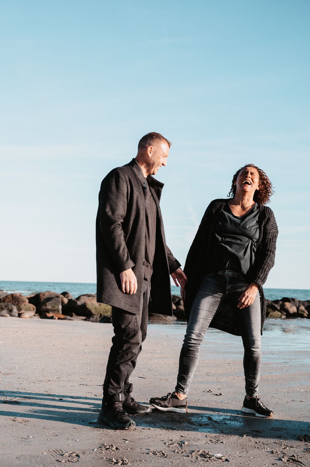 Lachendes Paar am Strand in Dänemark, Hand in Hand, voller Freude und Bewegung, farbiges Pärchenshooting