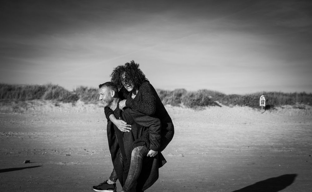 Schwarz-Weiß: Paar kuschelt eng am Strand, Naturlicht betont Emotion.