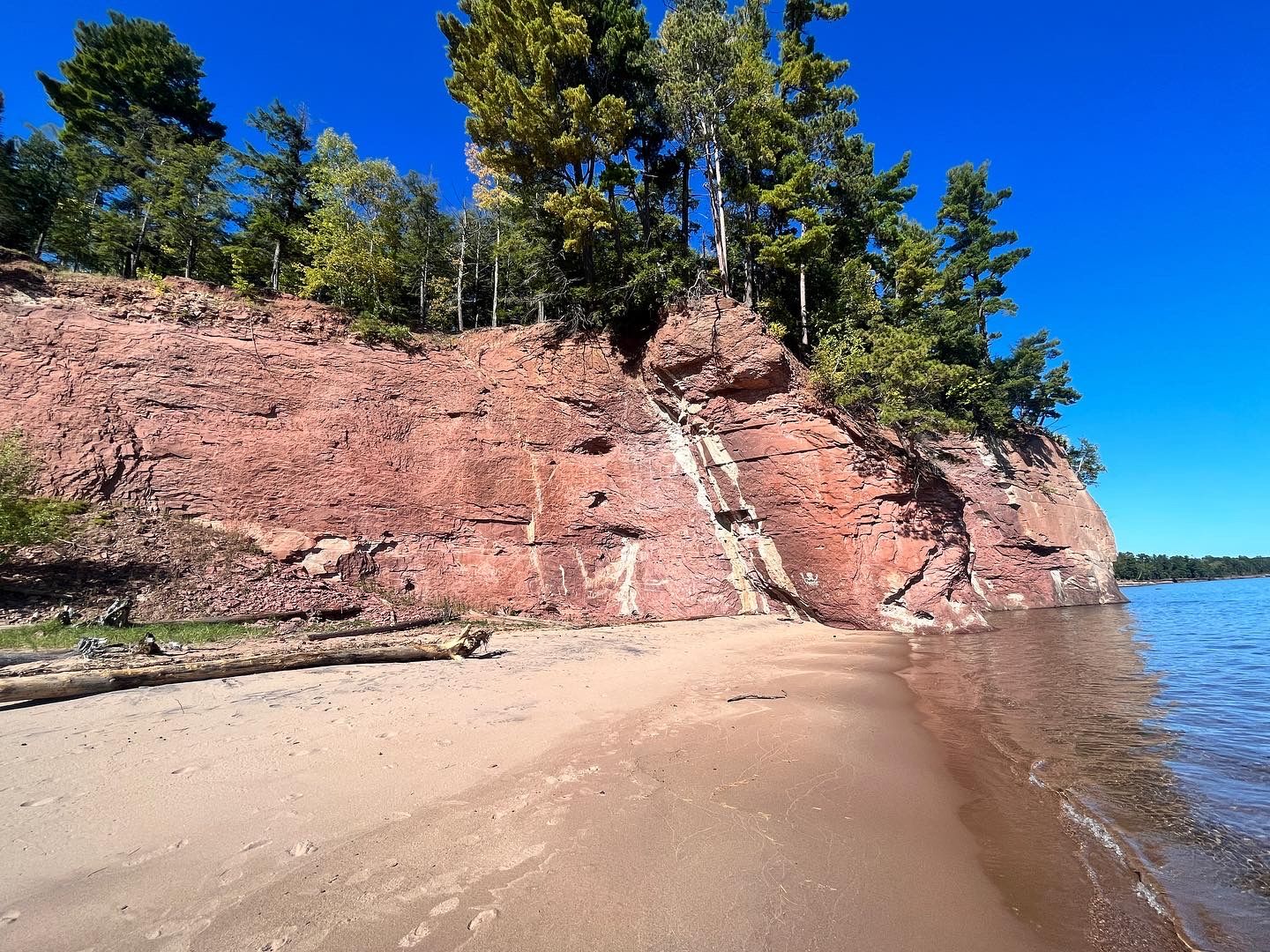 Turquoise waters meet steep cliffs covered in lush green forest along the scenic Pictured Rocks shoreline along Lake Superior in Michigan.