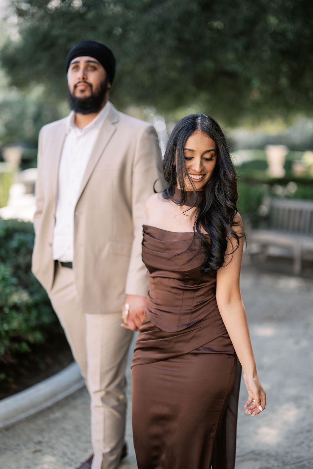 A romantic photoshoot in a garden setting featuring a couple in brown dress and beige suit.
