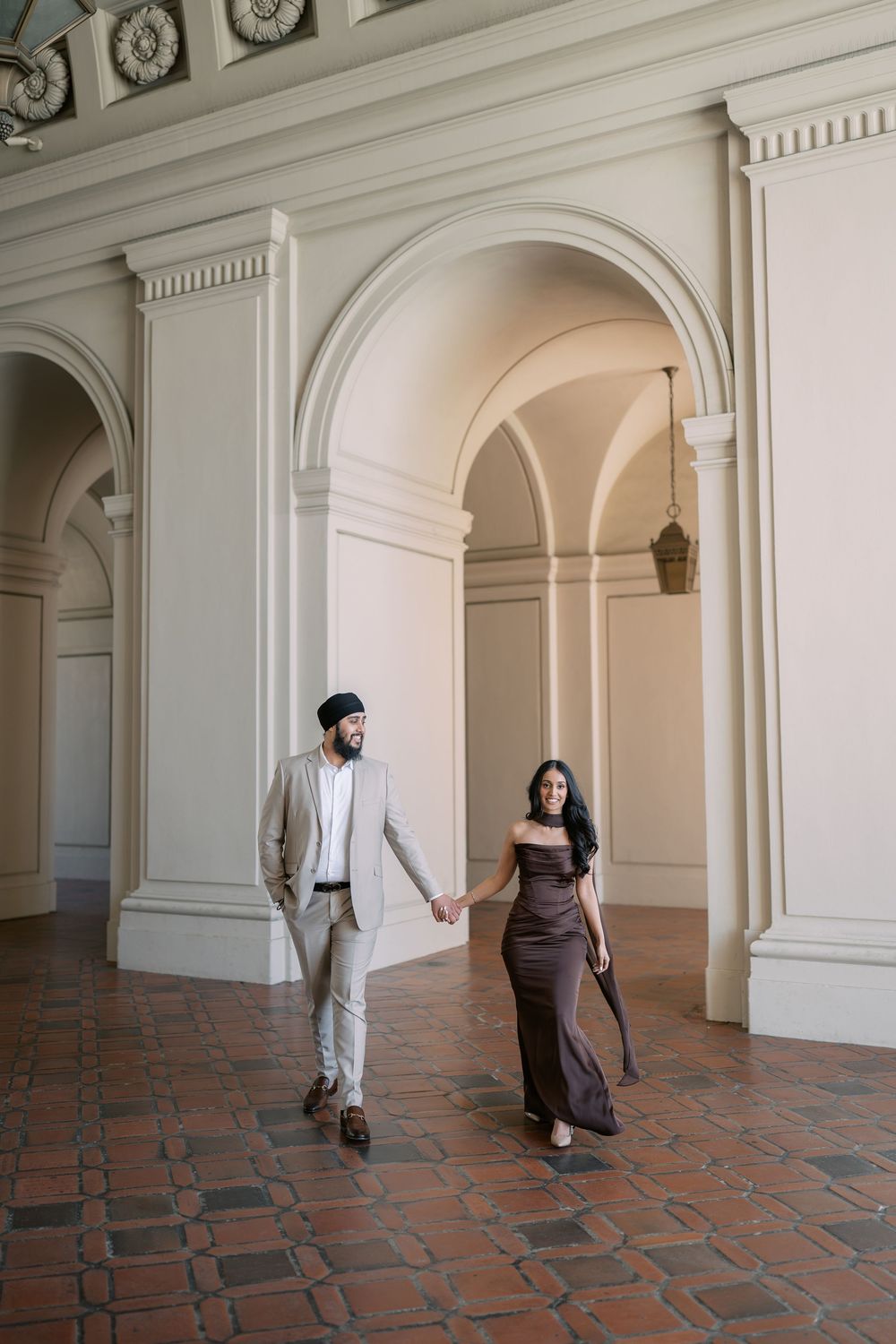 Couple walking together through elegant arched hallway with terracotta floors and classical white architectural details.