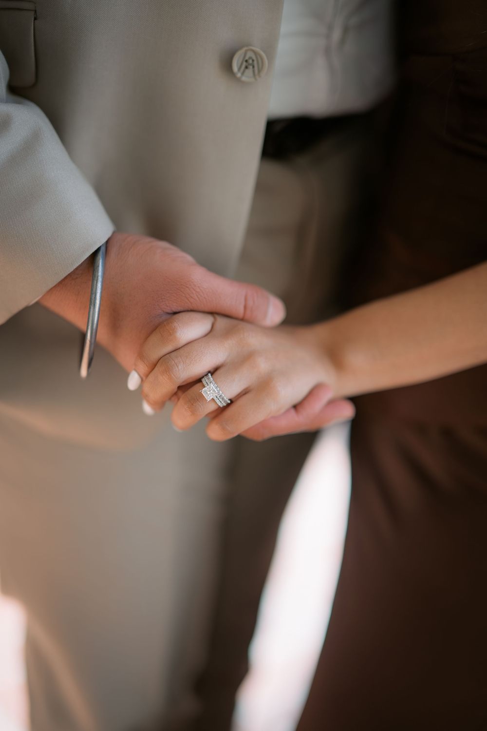 Close-up shot of hands holding with an engagement ring prominently displayed.