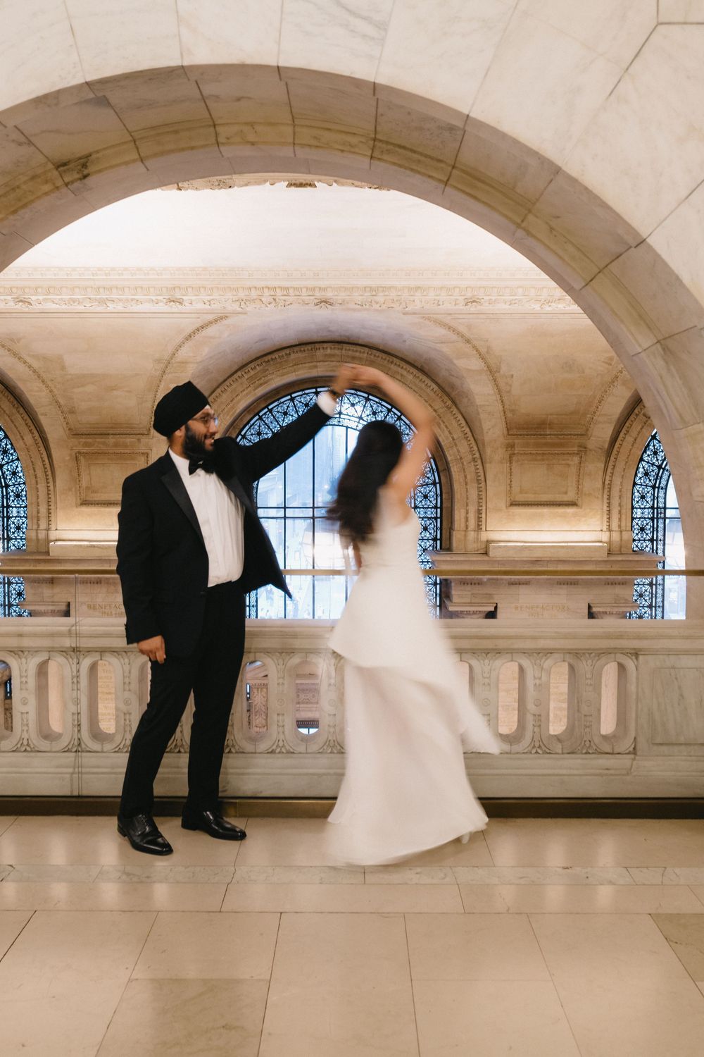A groom in a black turban twirls his bride in a white gown under an elegant marble arch.