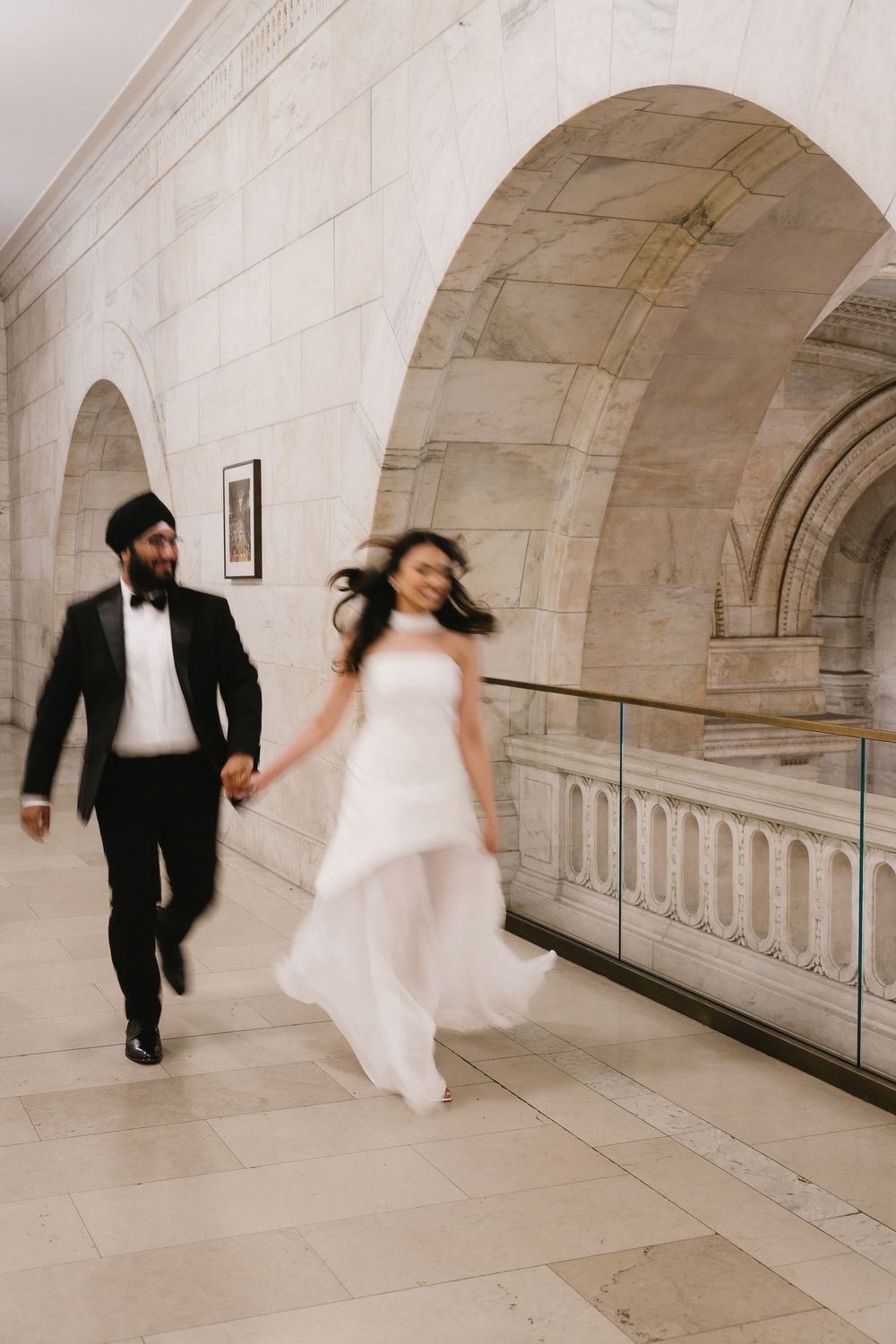 Bride and groom holding hands running through elegant stone archway corridor in wedding attire.