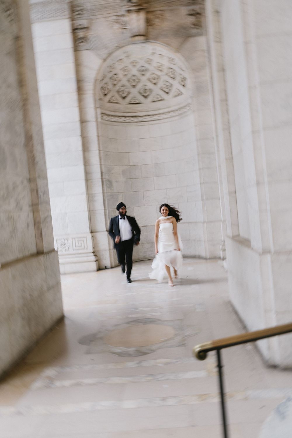 Bride and groom walking through elegant marble columns of a grand building during wedding photos.