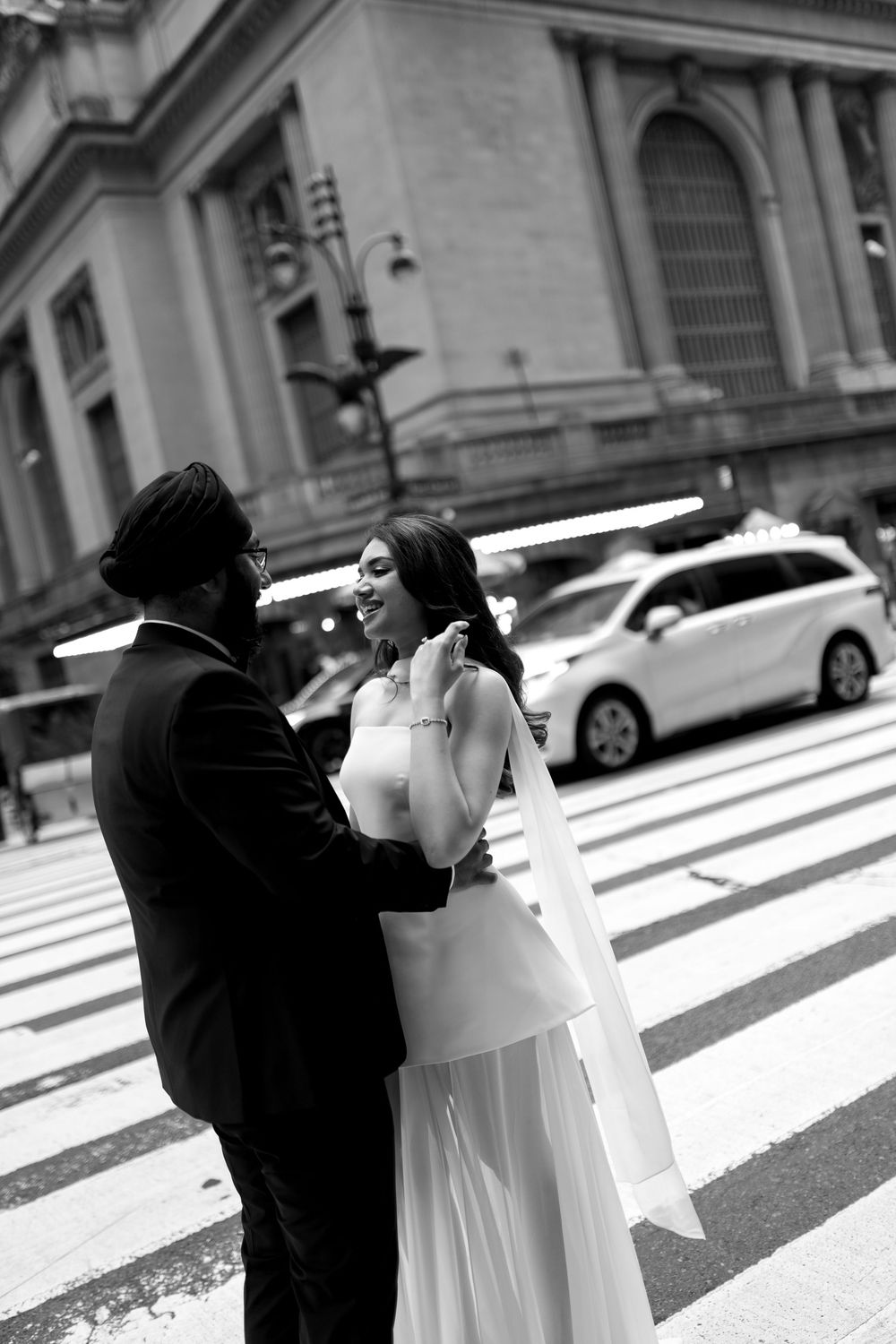 Sikh groom in turban holds smiling bride in white dress near Grand Central Terminal, black and white.