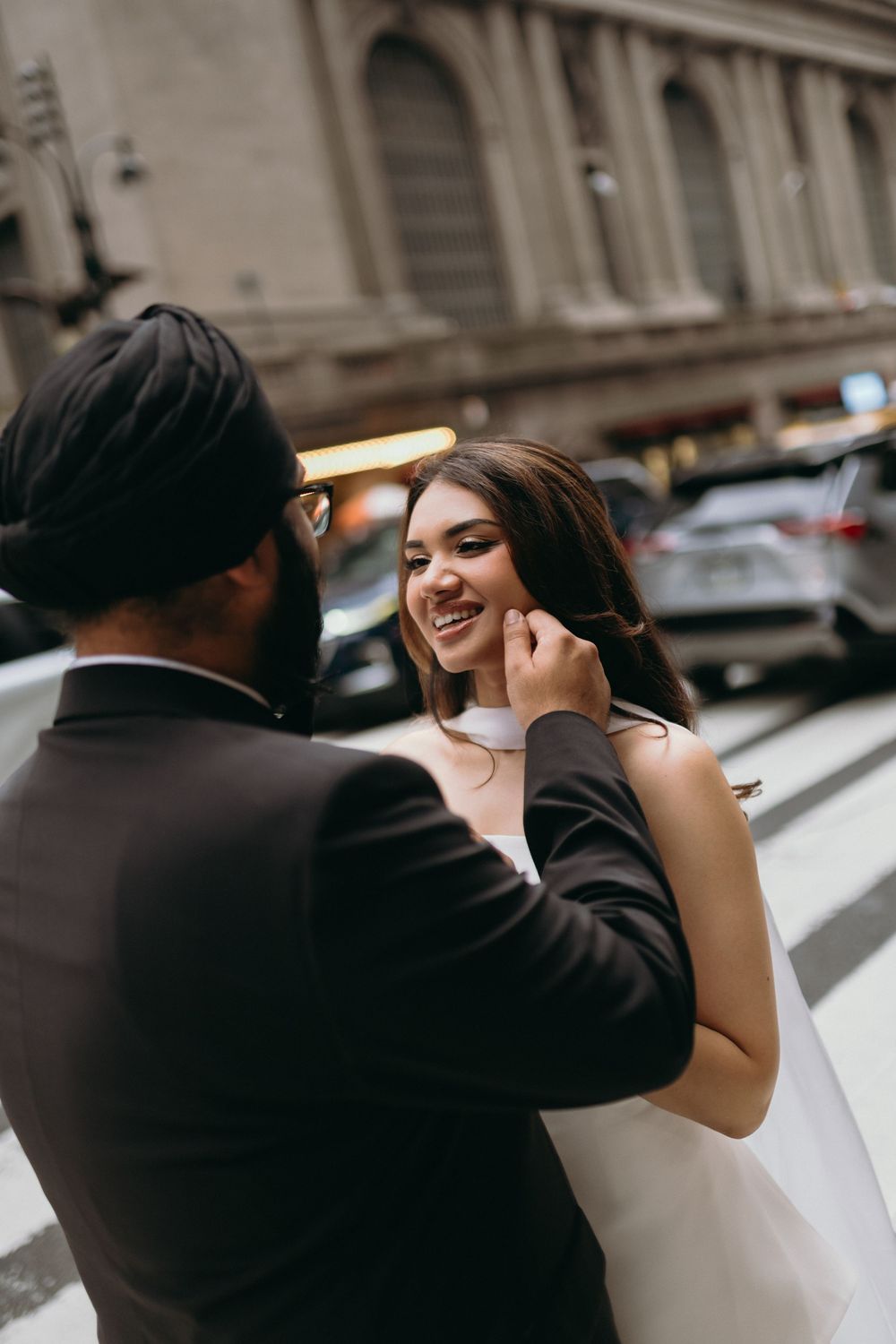 Smiling bride gazes at groom as he tenderly touches her face on a New York City street.