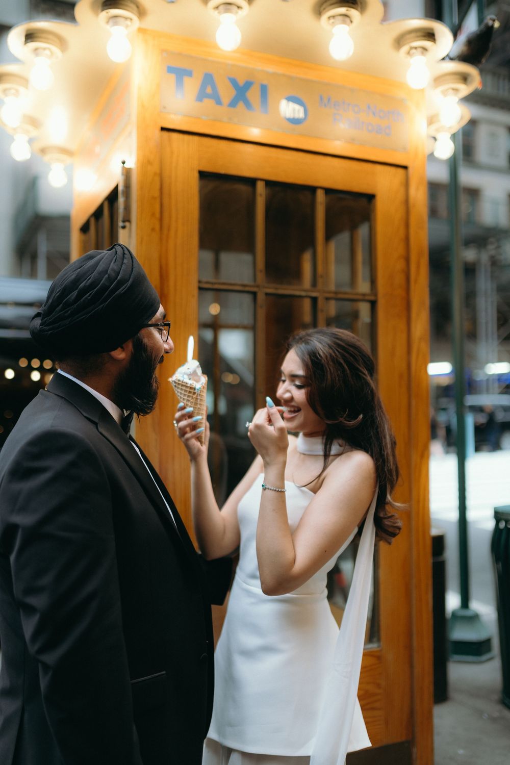 Newlyweds enjoy ice cream together outside a taxi booth in New York City after their wedding.