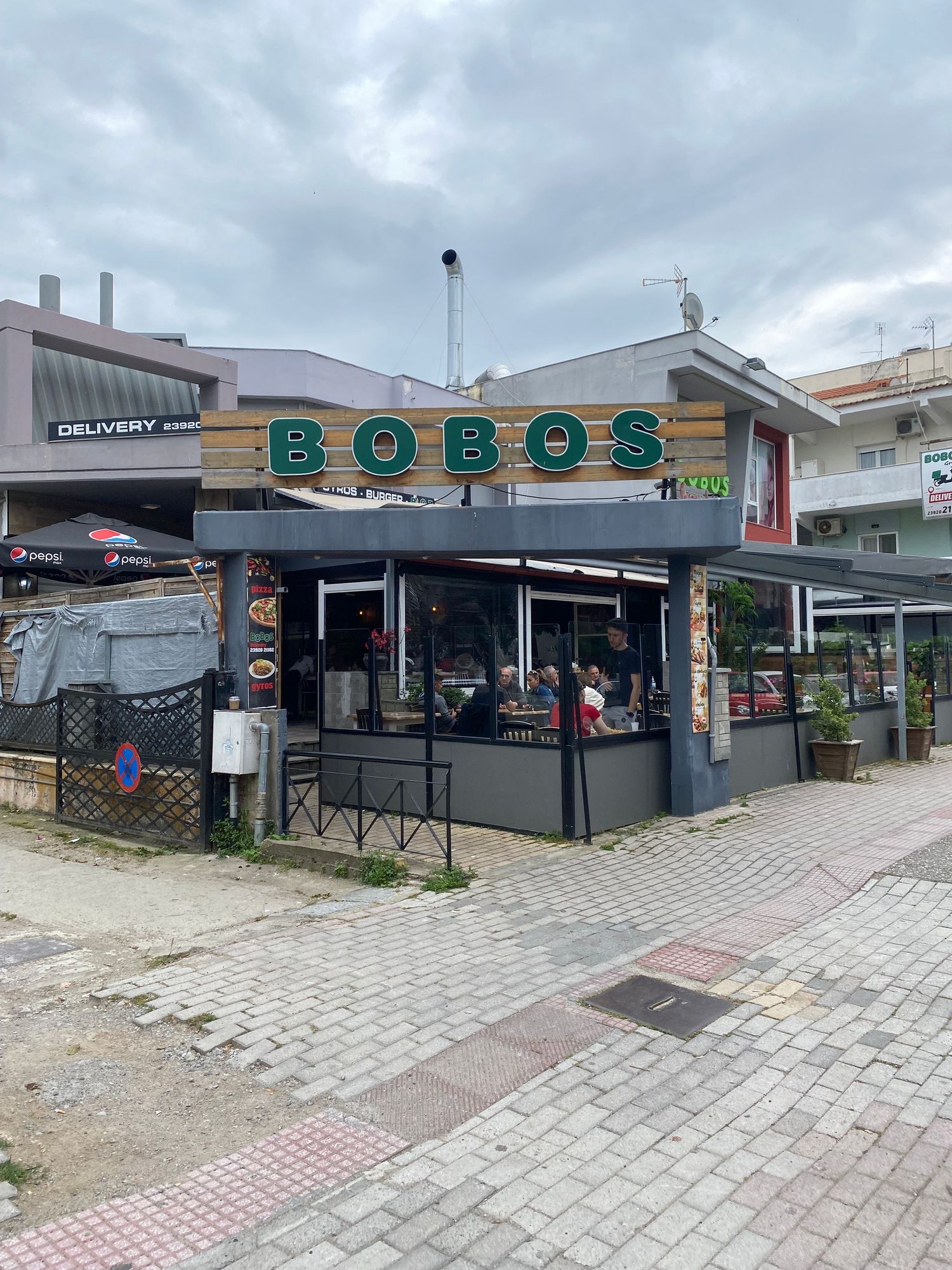 Exterior view of Bobos restaurant storefront with green signage and outdoor seating area on a cobblestone street.