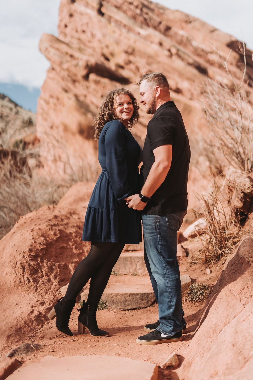 A couple shares a romantic moment against red rock formations in a desert landscape during a photo session.