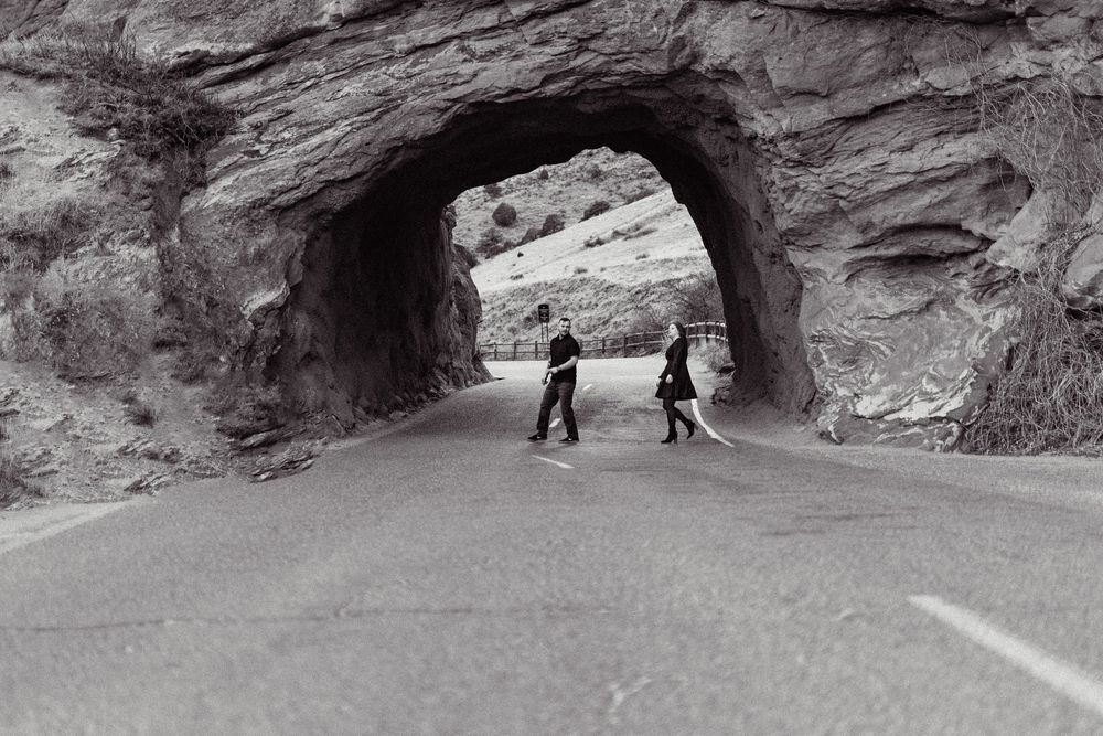 Two silhouetted figures walking through a natural stone tunnel carved into a rocky cliff face.