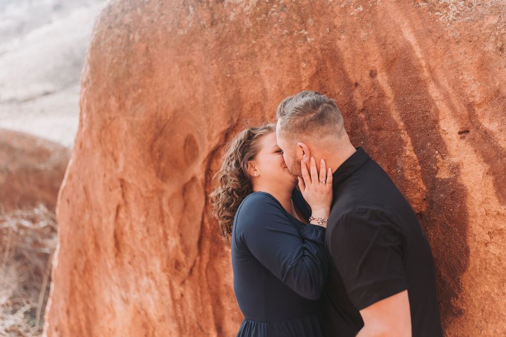 A romantic couple embraces against vibrant red rock formations in a desert landscape.