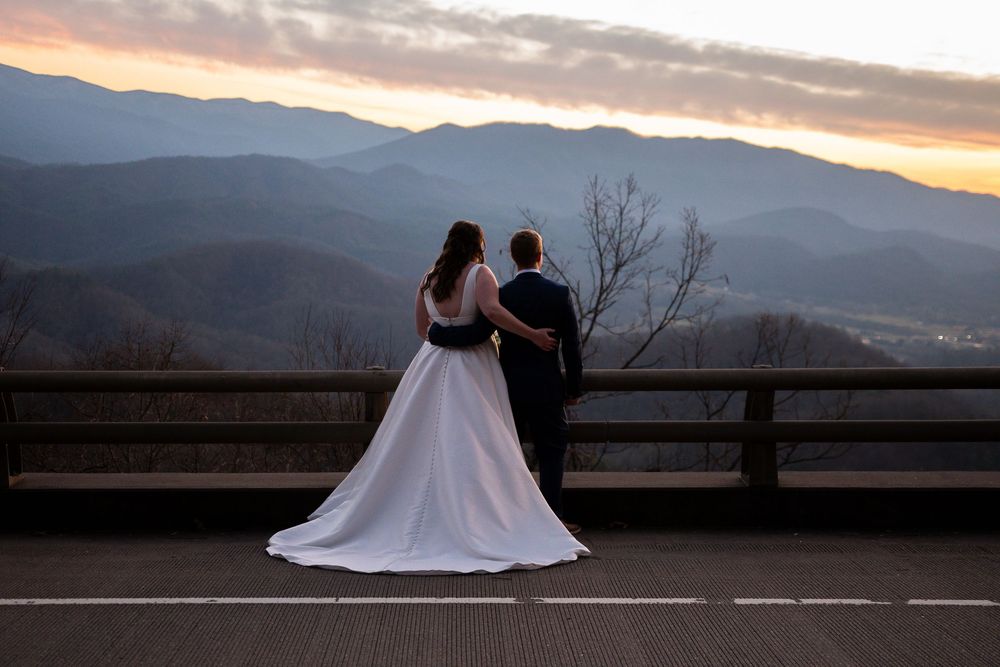 A wedding couple silhouetted against a dramatic mountain sunset with a long flowing white dress.
