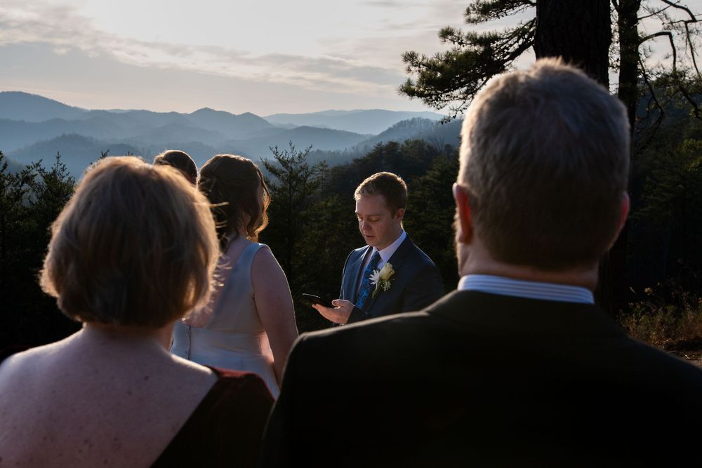 Silhouettes of people gathered at a scenic mountain overlook during dusk.