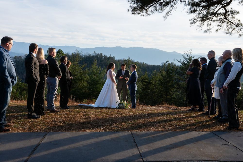 A group gathers for an outdoor ceremony on a mountaintop with distant peaks in view.
