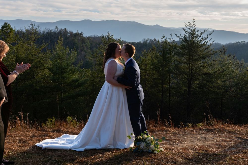A couple shares an intimate moment during their wedding photoshoot against a backdrop of mountain vistas and evergreen trees.