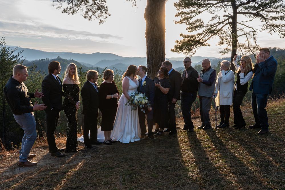 Wedding guests stand in a line at sunset creating long shadows across a mountain overlook.