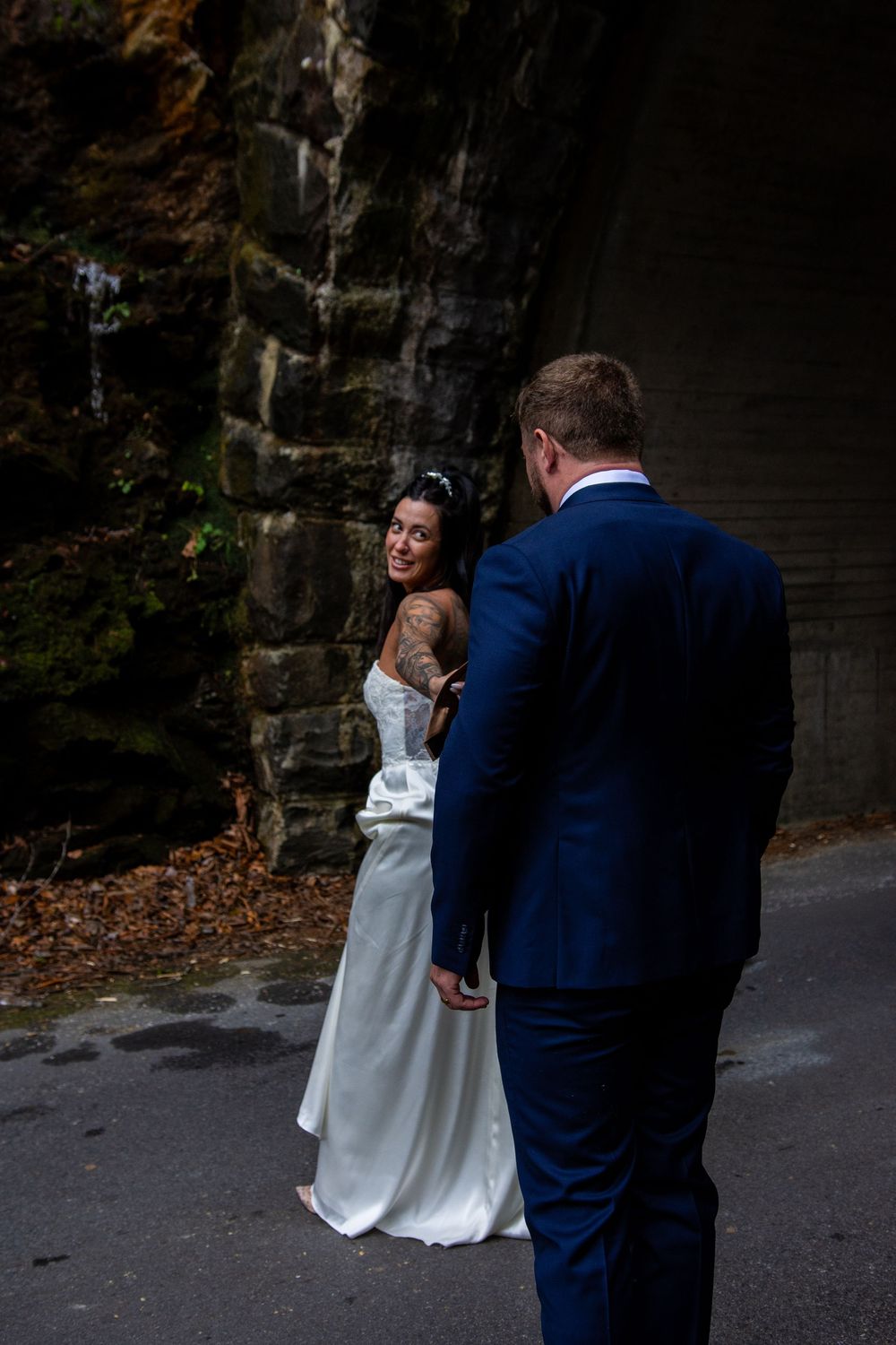 A couple in wedding attire shares an intimate moment against a stone wall backdrop in a romantic outdoor setting.