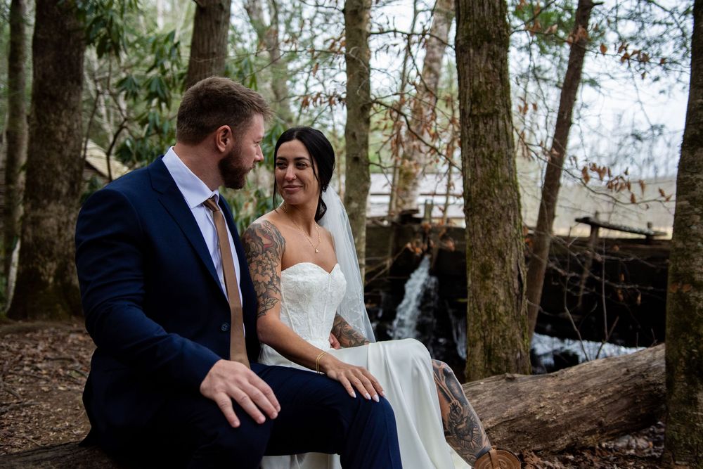 A couple in wedding attire shares a romantic moment together in a wooded forest setting.