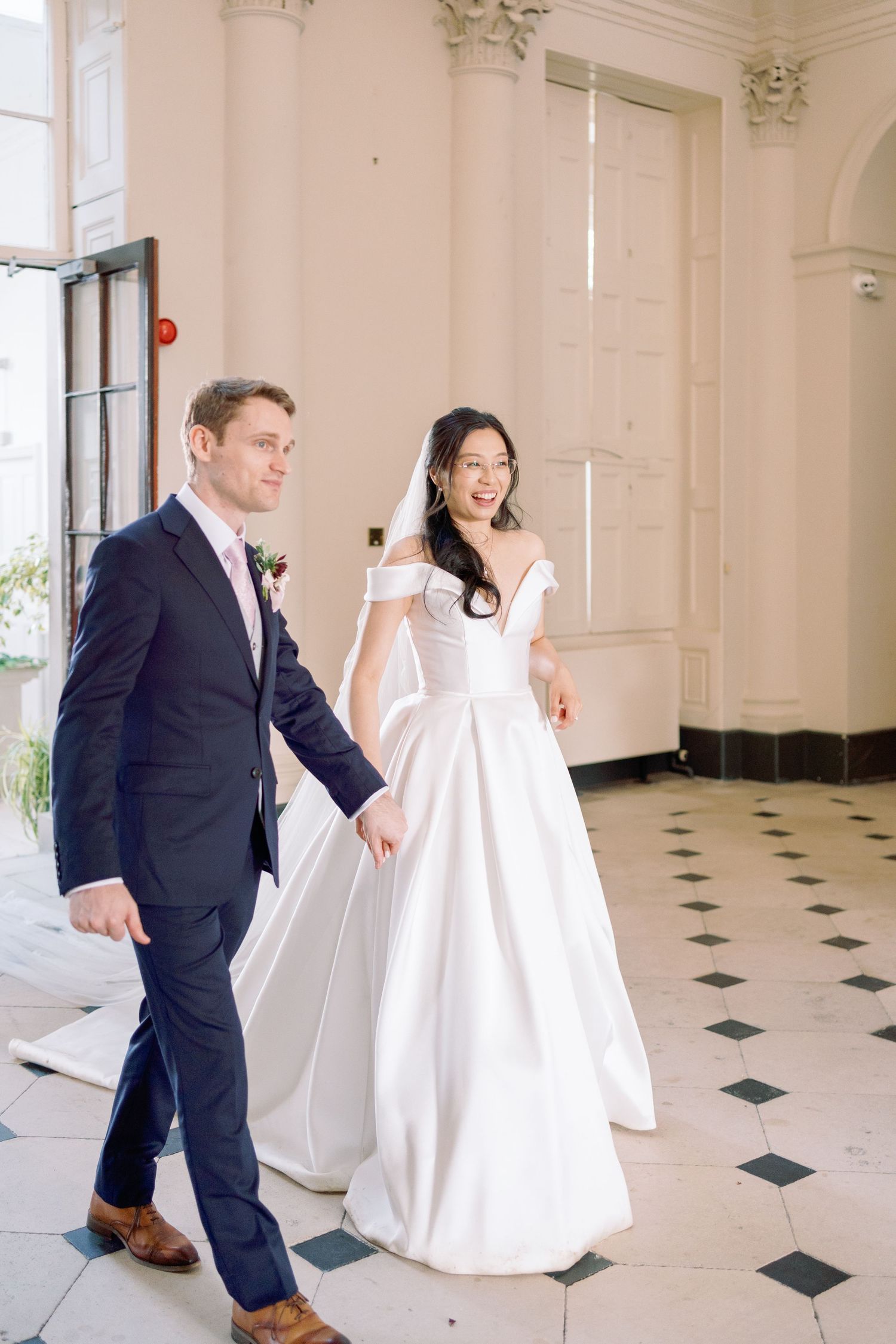 A couple in wedding attire dances and twirls together in a grand room with black and white checkered floors.