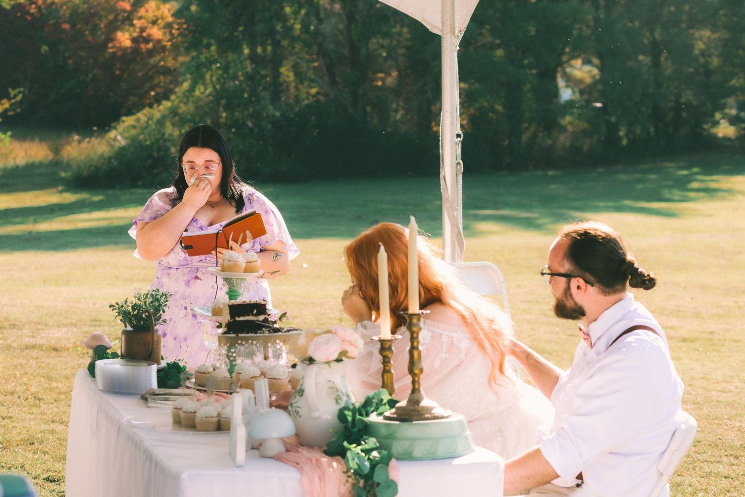 A group of people enjoy tea and snacks at an outdoor garden party table during golden hour.