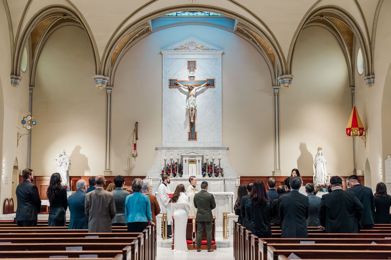 Interior view of a Catholic church sanctuary with vaulted ceilings, pews, and religious statues along the walls.
