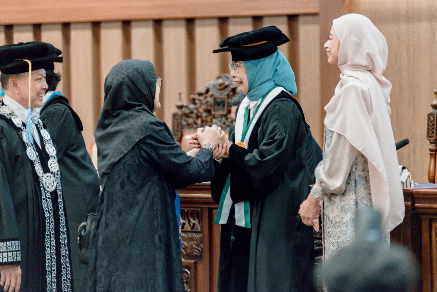 Graduates in black caps and gowns stand in line during a formal commencement ceremony.