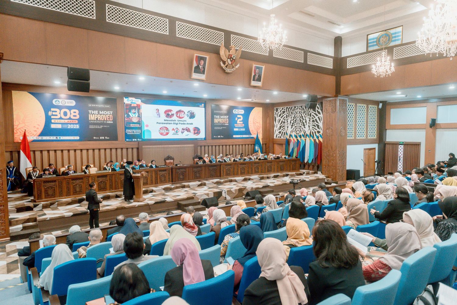 A large conference room filled with attendees in blue chairs during a professional gathering or seminar.