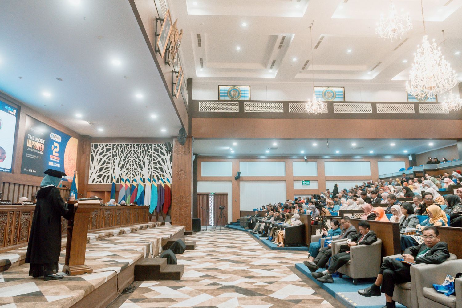 Interior view of a modern conference hall with tiered seating and recessed lighting in warm tones.