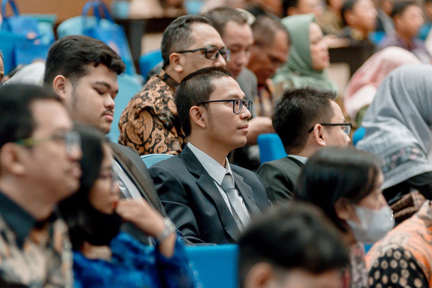 A large crowd of spectators in formal attire watches intently during what appears to be a professional event or conference.