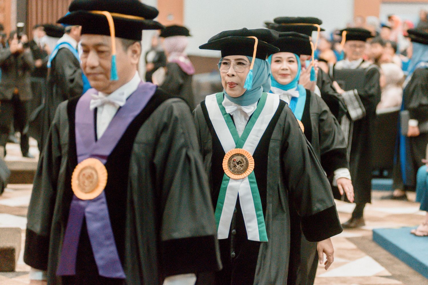 Academic procession of graduates in traditional caps and gowns with ceremonial medallions at university commencement.
