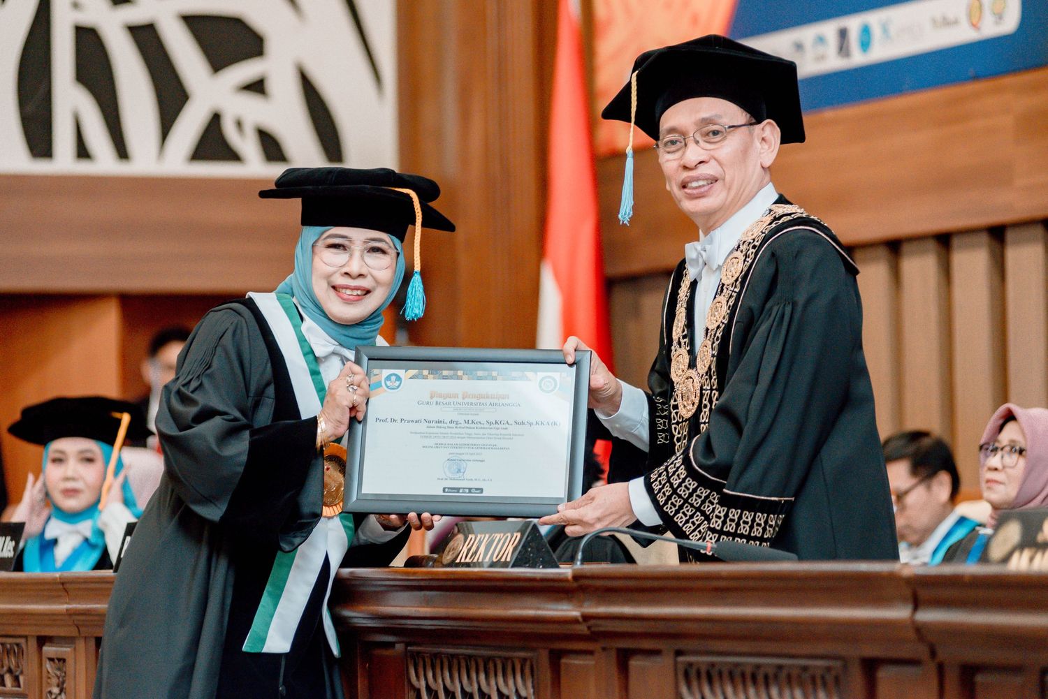 Graduate students in black caps and gowns receiving diplomas during university commencement ceremony.