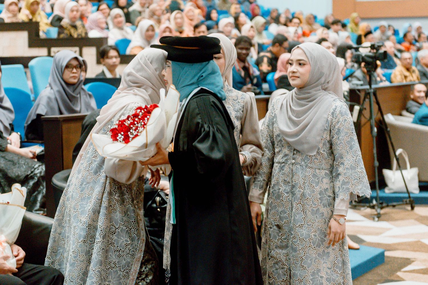 Group of women in traditional hijabs and elegant gowns celebrate at a formal gathering in an event hall.