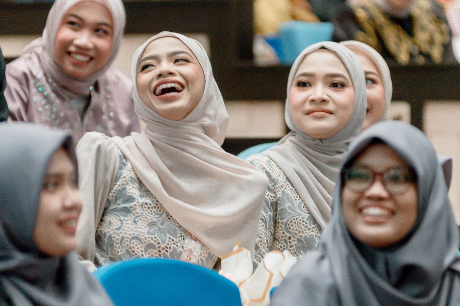 A group of women wearing hijabs in neutral tones smile and laugh together during a joyful gathering.