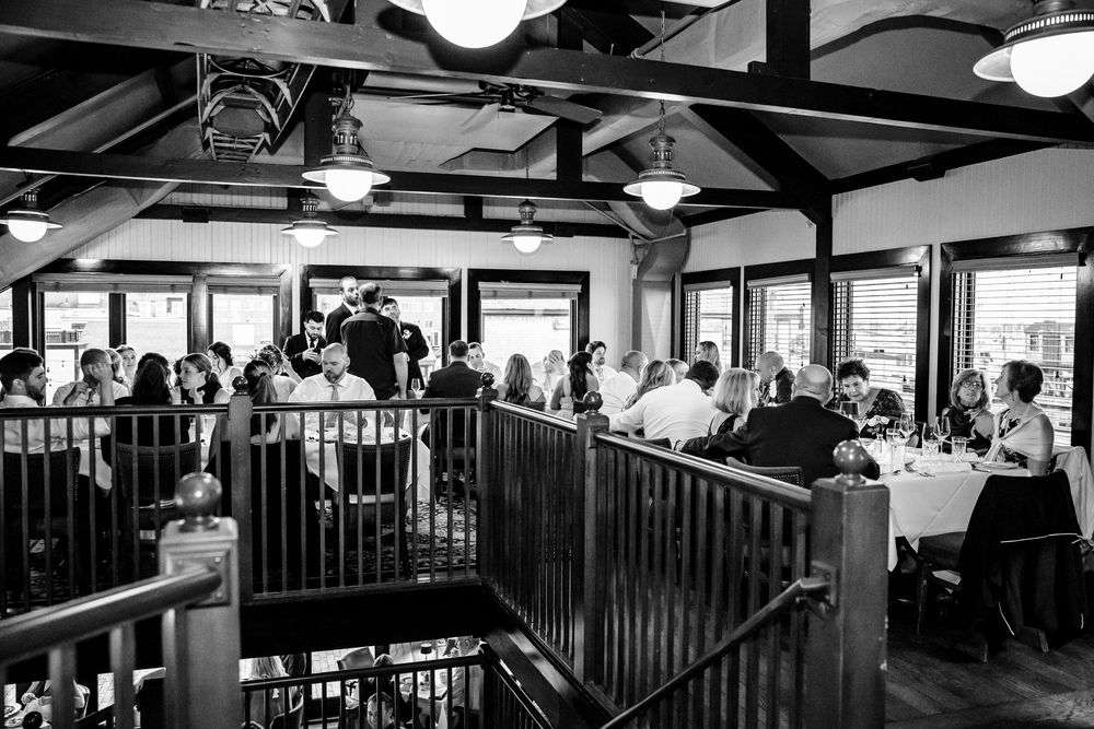Diners enjoy a meal in a rustic restaurant with wooden beams and large windows overlooking a scenic view.