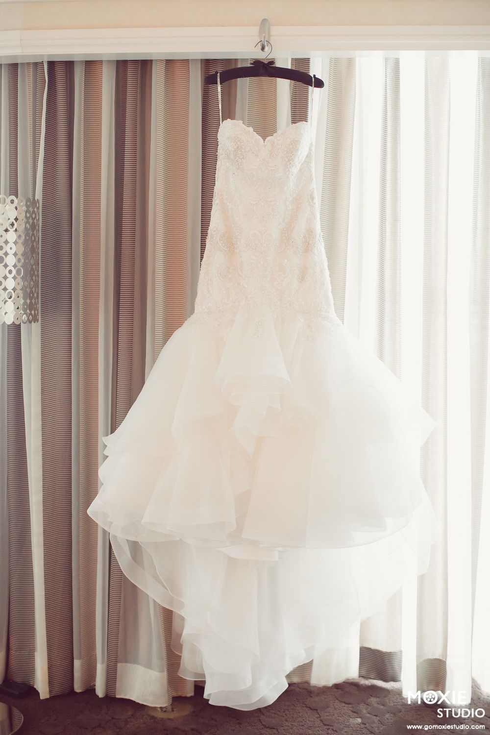 White wedding dresses hanging in a row against a window with soft natural light creating an ethereal display.