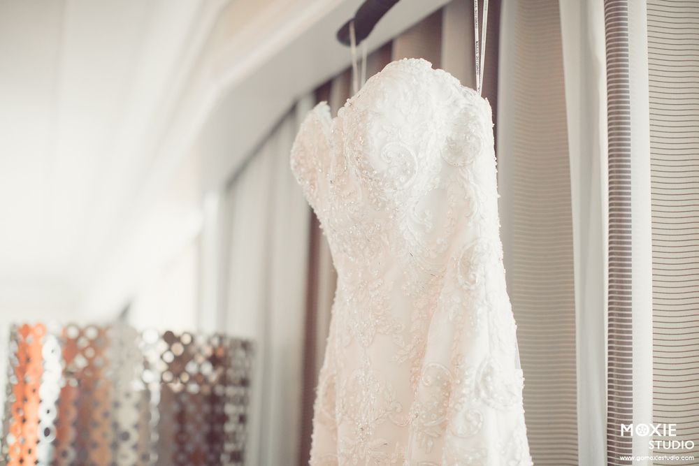 Three elegant white wedding dresses hanging on display in a bridal boutique with soft natural lighting.