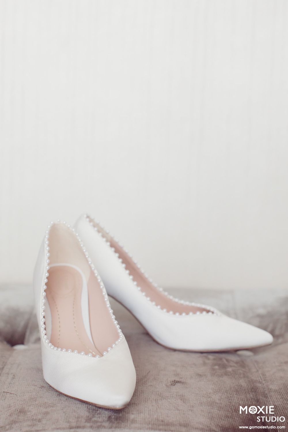 Elegant white bridal shoes with pointed toes arranged artistically on a neutral surface.