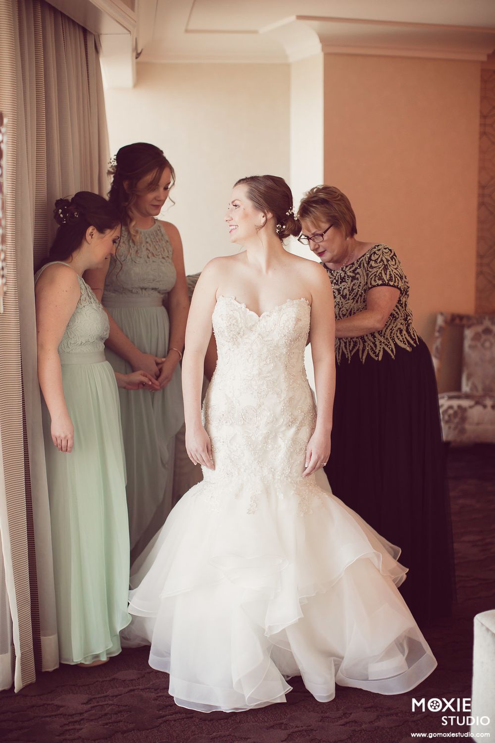 Bridesmaids in mint green dresses help adjust the bride's flowing white wedding gown during pre-ceremony preparations.