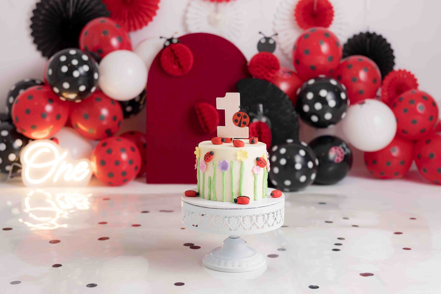 A birthday cake with red, black and white balloon decorations and party lights in a festive party setting.