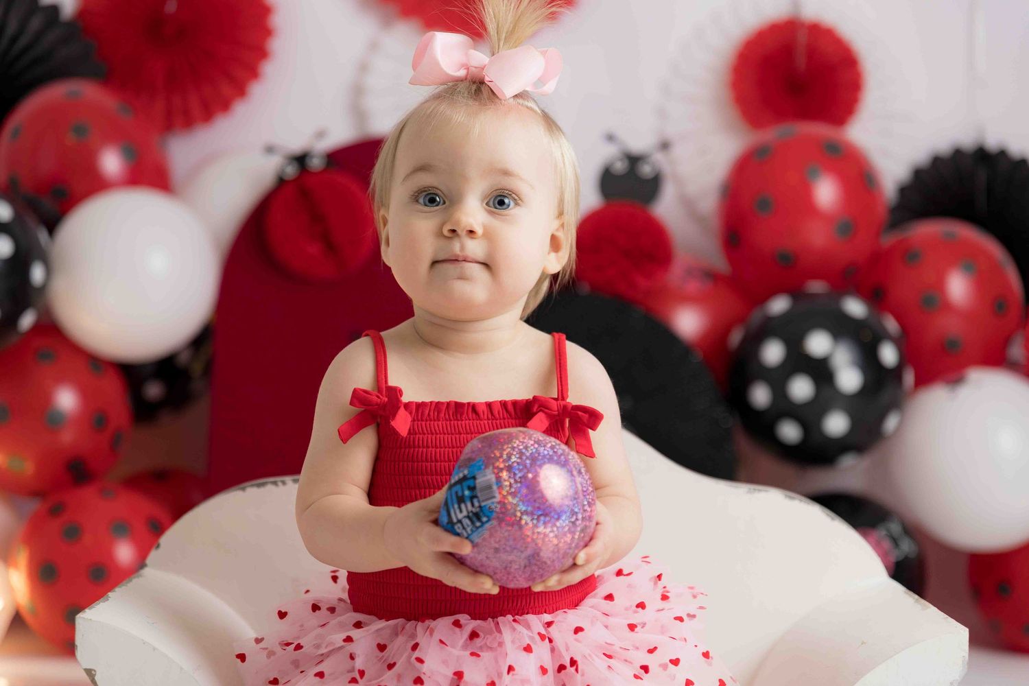 Red and white polka dot themed cake smash photo session with balloons and decorative backdrop for first birthday celebration.