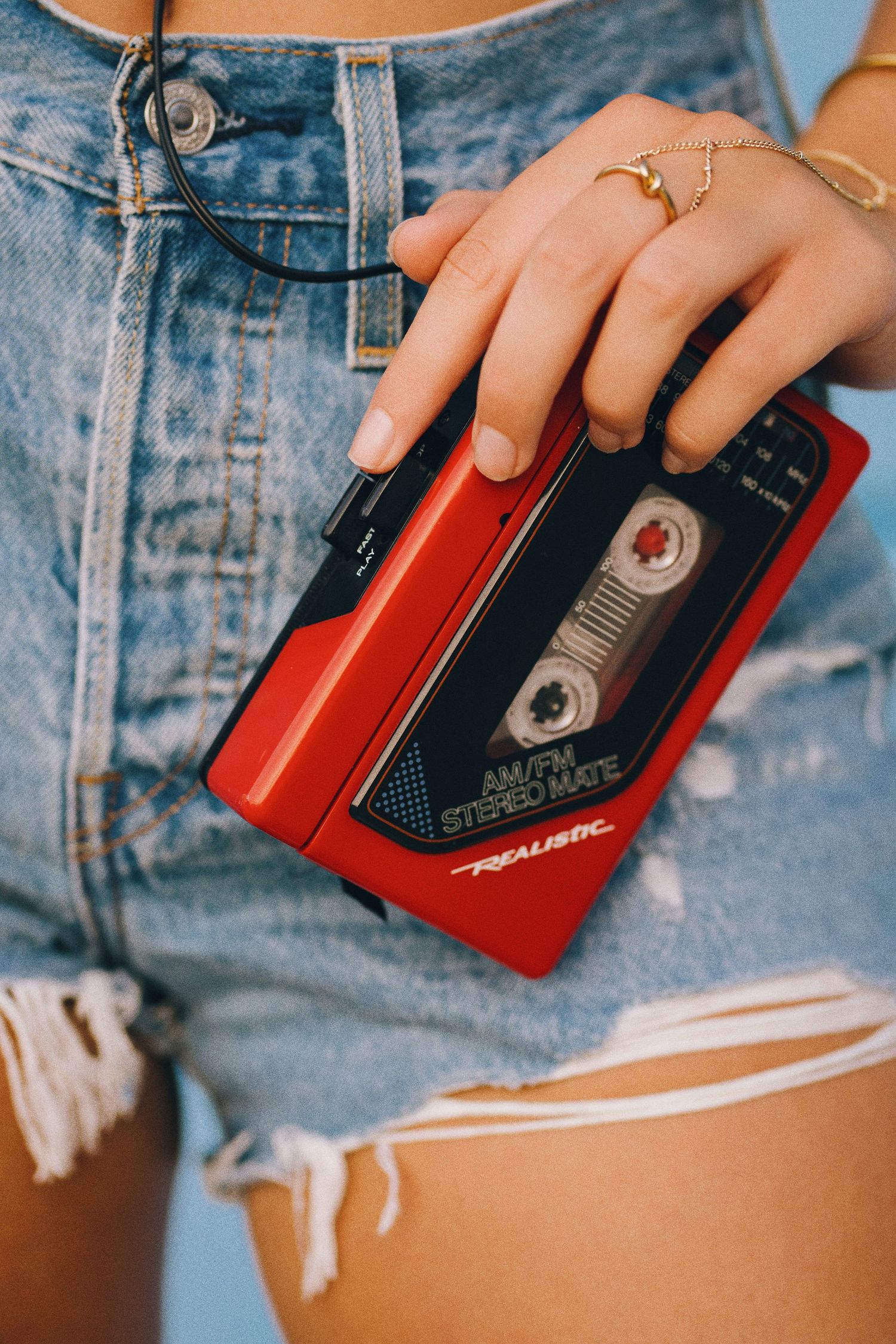 Close-up shots of hands holding a red vintage cassette player against denim shorts background.