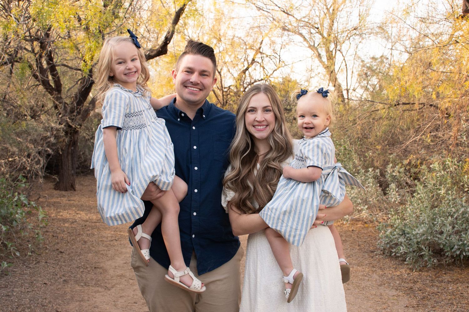 Family portrait session in a park during autumn with golden foliage and warm sunlight creating a cozy atmosphere.