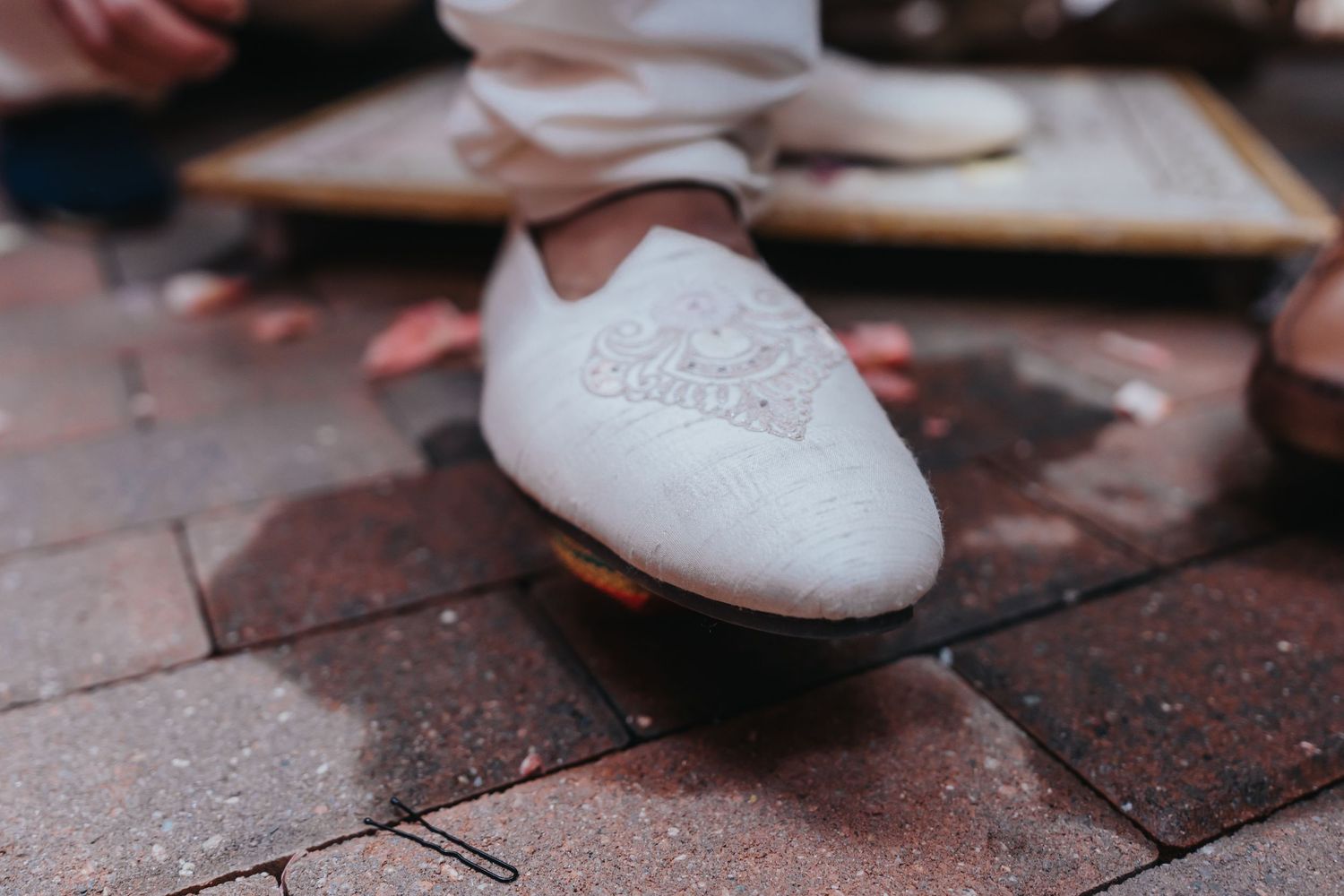 Memory Lane Studios bridal detail close-up of elegant white wedding shoes on brick pavement by luxury wedding photographer Tharun Palla