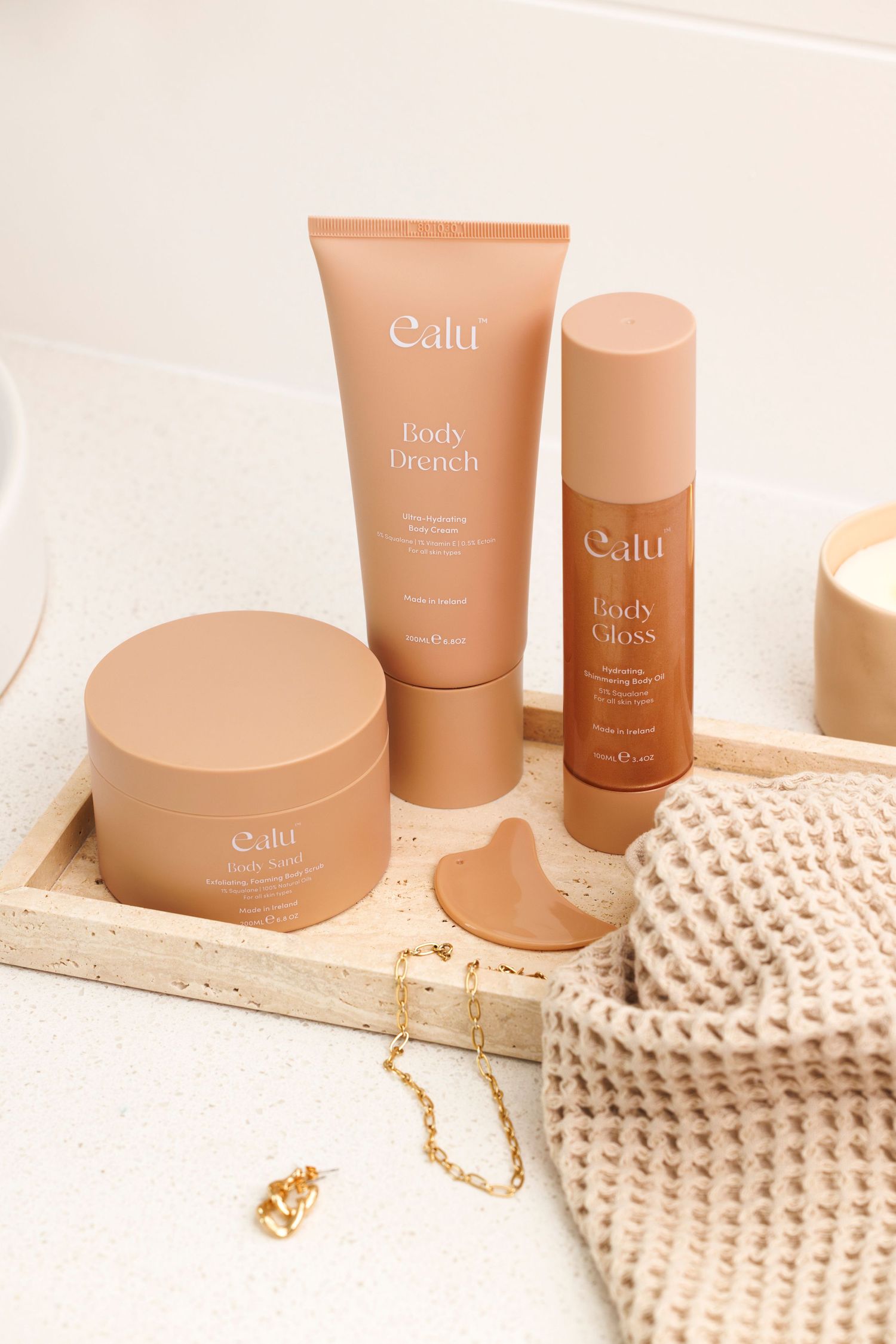 Peach-colored beauty and skincare products from Calu arranged with knit accessories and jewelry on light surface.