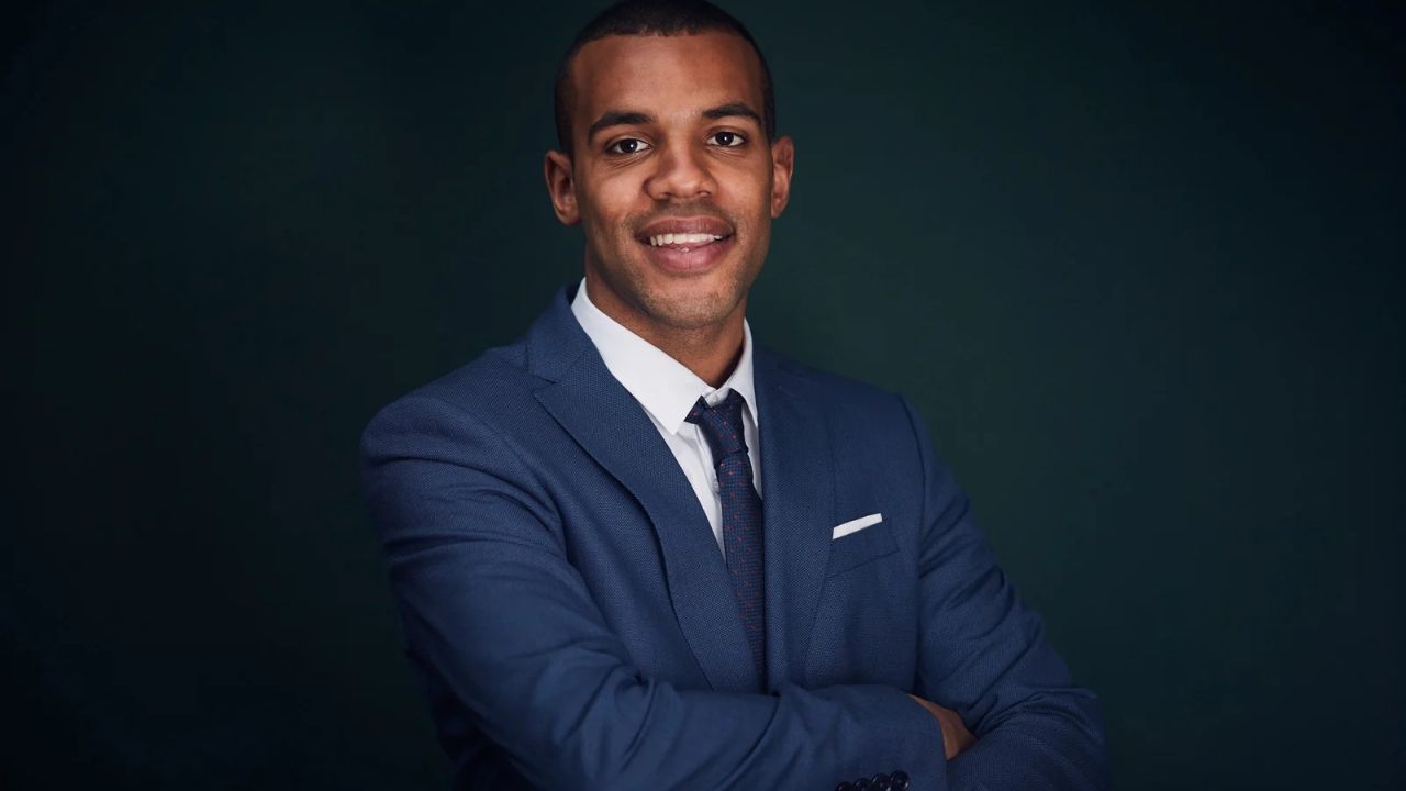 A black professional man with blue suit and blue tie and a warm smile